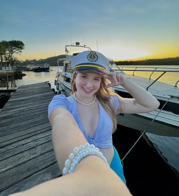 Lívia Dall'Acqua de quepe de comandante, num píer ao pôr do sol