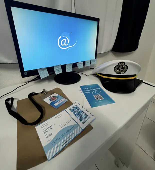 Mesa com o monitor da Acqua Digital, o quepe de comandante, o crachá e os materiais de embarque digital